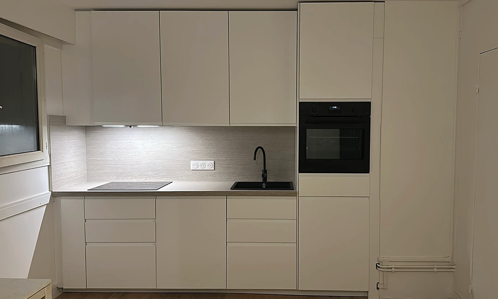 Cuisine blanche épurée sans poignées, colonne four noire, crédence effet bois